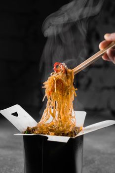 Steaming rice noodles in wok box on black background. Fast food delivery service. Takeaway chinese street meal. Udon in black food container