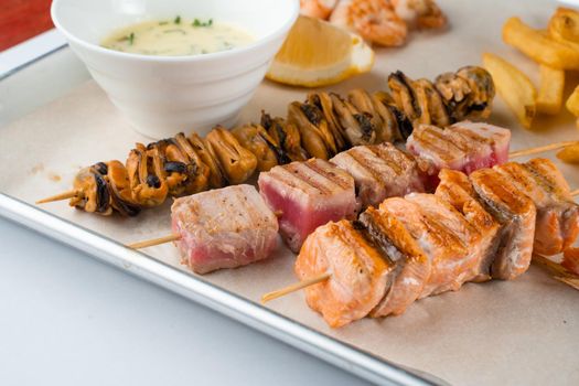 Barbecue seafood kebab with grilled mussels, tuna, salmon on a wooden skewer with white sauce and lemon.