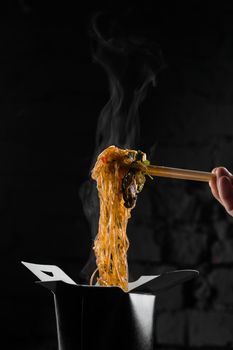 Steaming rice noodles in wok box on black background. Fast food delivery service. Takeaway chinese street meal. Udon in black food container