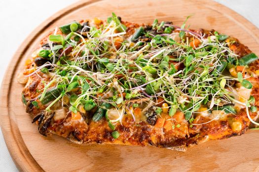 Vegan pinsa romana with mushrooms, asparagus, corn, peas, carrots, cheese and sauce, garnished with microgreens on wooden board.