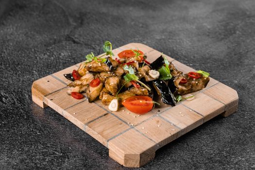 Fried eggplants on a wooden board, decorated with chili, garlic, cilantro, sesame seeds on a gray background