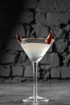 Cocktail in glass with chili on gray background. Devil alcohol drink