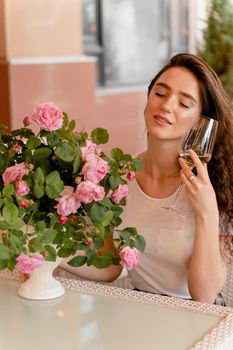 Dreaming woman with glass of alcoholic white wine in cafe in summer terrace and bouquet of roses on the table