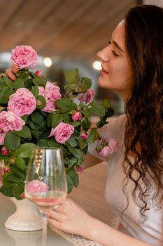 Dreaming woman with glass of alcoholic white wine in cafe in summer terrace and bouquet of roses on the table