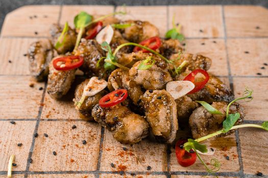 Fried mussels with chili, garlic, sesame, herbs, on square wooden board on gray background