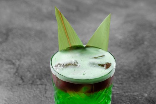 Green layered cocktail decorated with bamboo leaves on a gray background