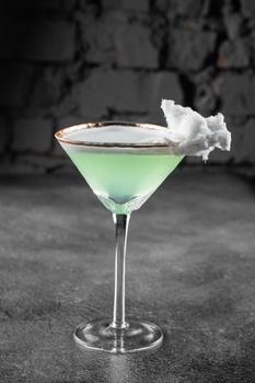 Green alcohol cocktail in a glass decorated with cotton candy on gray background