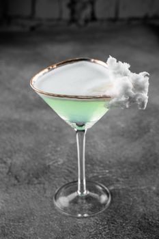 Green alcohol cocktail in a glass decorated with cotton candy on gray background