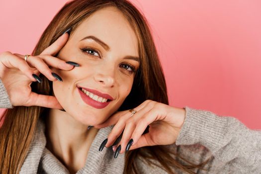 Close-up beauty portrait of a woman weared grey sweater on pink background. Professional model posing in studio. Lifestyle of caucasian happy girl.