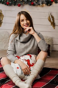 Young woman smiling in new year decoration. Christmas celebration. Attractive girl weared in warm woolen sweater and socks.