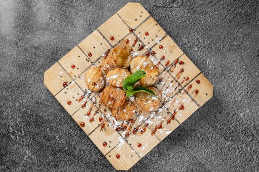 Rice crackers with maple syrup and powdered sugar garnished with mint on square wooden board on gray background. Deep-fried biscuits