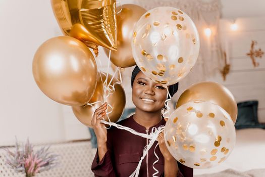 Muslim new year party with golden balloons for black woman. African attractive girl celebration of the end of year. Happy emotion