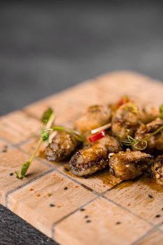 Fried mussels with chili, garlic, sesame, herbs, on square wooden board on gray background