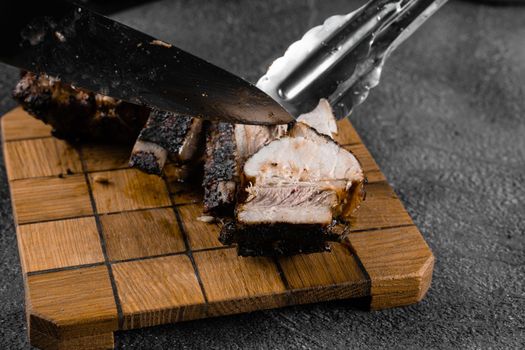 Grilled ribs slicing on a wooden plate on a gray background. Barbecue decoration