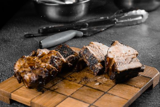 Grilled ribs slicing on a wooden plate on a gray background. Barbecue decoration