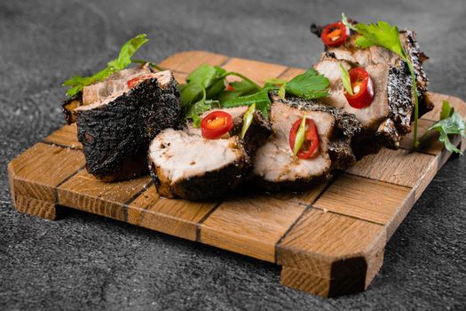 Fried ribs on a wooden plate on a gray background. Barbecue decoration parsley and chili