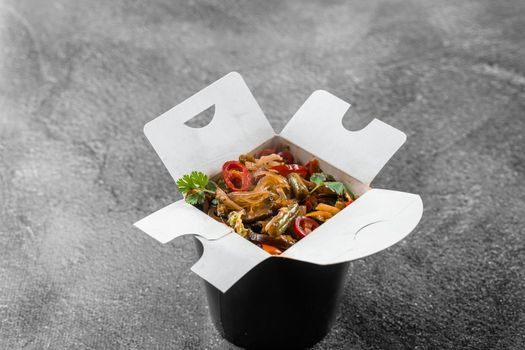 Wok in box rice noodles in black food container. Fast food delivery service. Takeaway chinese street meal