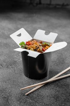 Wok in box rice noodles in black food container. Fast food delivery service. Takeaway chinese street meal