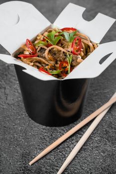 Wok in box spicy noodles in black food container. Fast food delivery service. Takeaway chinese street meal