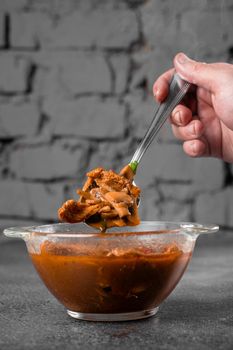 Soup with meat, mushrooms, tomatoes in transparent bowl on gray background. Appetizing thick satisfying tom yam