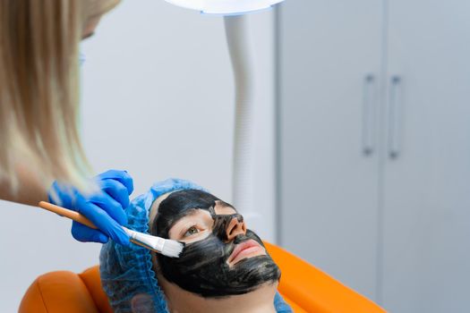 Dermatologist smears black mask on face for laser photorejuvenation and carbon peeling. Dermatology and cosmetology. Using surgical laser.