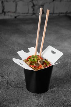 Wok in box spicy noodles in black food container. Fast food delivery service. Takeaway chinese street meal