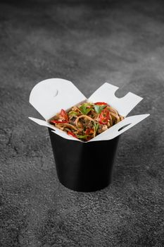 Wok in box spicy noodles in black food container. Fast food delivery service. Takeaway chinese street meal