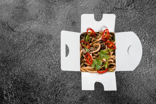 Wok in box spicy noodles in black food container. Fast food delivery service. Takeaway chinese street meal. Top view