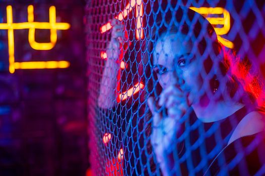 Caucasian woman in neon studio behind chain-link mesh