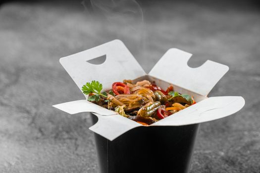 Wok in box rice noodles in black food container. Fast food delivery service. Takeaway chinese street meal