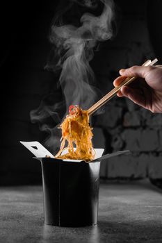 Steaming rice noodles in wok box on black background. Fast food delivery service. Takeaway chinese street meal. Udon in black food container