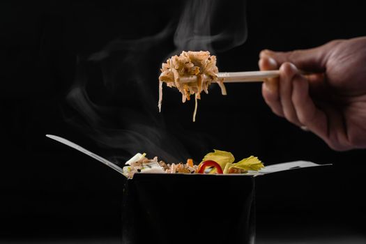 Steaming hot rice in wok box on black background. Holding rice with chinese chopsticks. Asian spicy dish for street restaurant and fast food delivery service