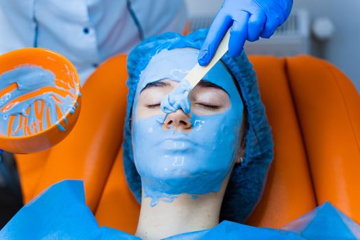 Alginate moisturizing mask for face and skin of young girl. Spa procedure for rejuvenation. beautician smears blue mask. Dermatology in medical clinic