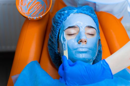 Alginate moisturizing mask for face and skin of young girl. Spa procedure for rejuvenation. beautician smears blue mask. Dermatology in medical clinic