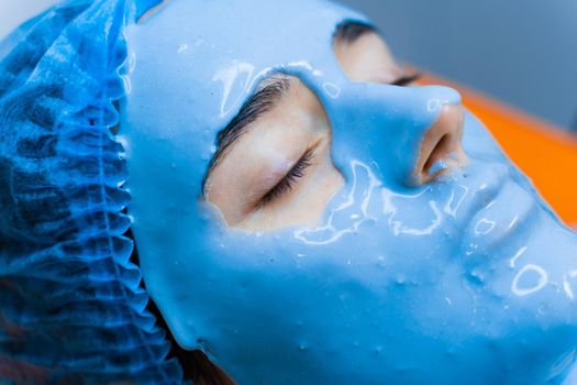 Alginate moisturizing mask for face and skin of young girl. Spa procedure for rejuvenation. beautician smears blue mask. Dermatology in medical clinic