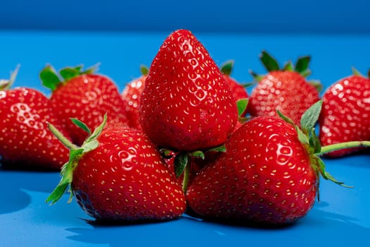 Bunch of strawberries on blue background. Red berry summer seasonal fruit