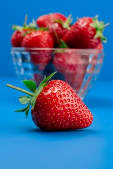 Bunch of strawberry in bowl on blue background. Yummy summer fruit