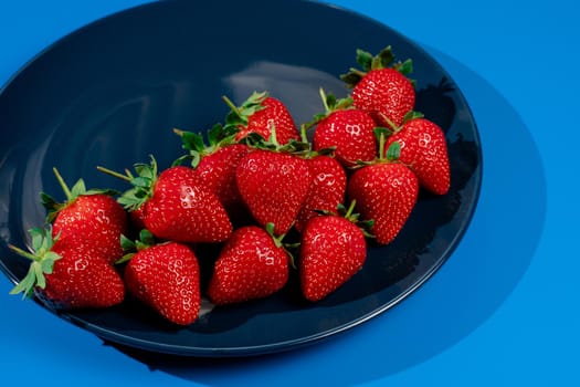 Bunch of strawberry on plate on blue background. Summer seasonal red berry