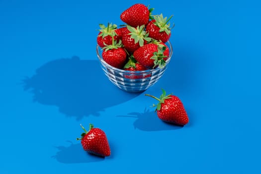 Bunch of strawberry in bowl on blue background. Yummy summer fruit