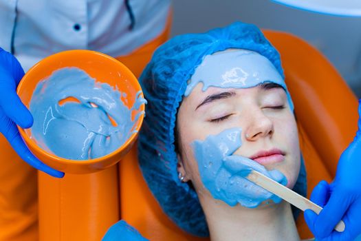 Alginate moisturizing mask for face and skin of young girl. Spa procedure for rejuvenation. beautician smears blue mask. Dermatology in medical clinic