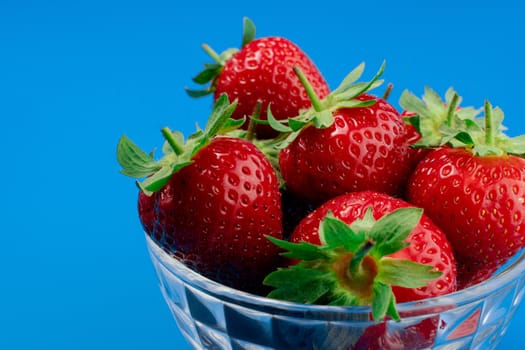 Bunch of strawberry in bowl on blue background. Yummy summer fruit