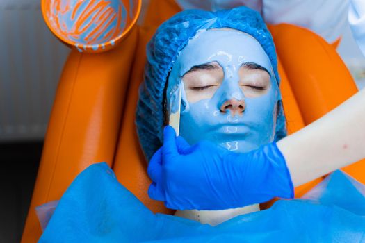 Alginate moisturizing mask for face and skin of young girl. Spa procedure for rejuvenation. beautician smears blue mask. Dermatology in medical clinic