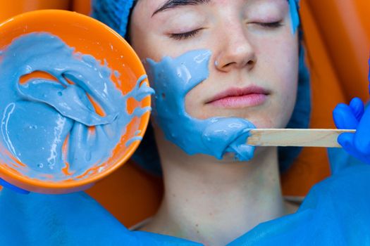 Alginate moisturizing mask for face and skin of young girl. Spa procedure for rejuvenation. beautician smears blue mask. Dermatology in medical clinic