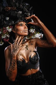 Portrait of a model in a headdress and dress made of coal. Bright makeup and body art.