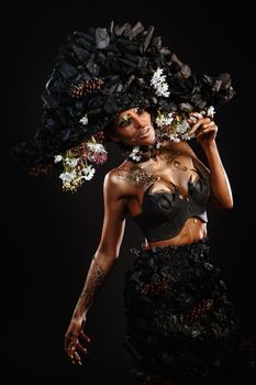 Portrait of a model in a headdress and dress made of coal. Bright makeup and body art.