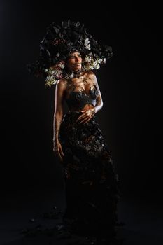 Portrait of a model in a headdress and dress made of coal. Bright makeup and body art.