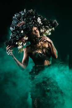 Portrait of a model in a headdress and dress made of coal. There is green smoke behind the model.