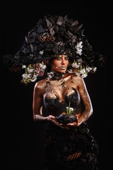 Portrait of a model in a headdress and dress made of coal. A stone with flowers in his hands