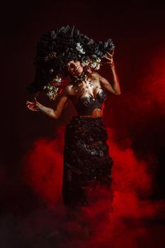 Portrait of a model in a headdress and dress made of coal. There is red smoke behind the model.