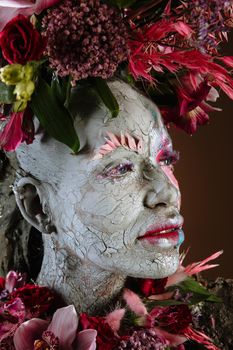 A girl smeared with clay. The model has a headdress made of flowers.